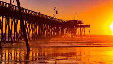 The pismo beach pier glows orange with the sunset.