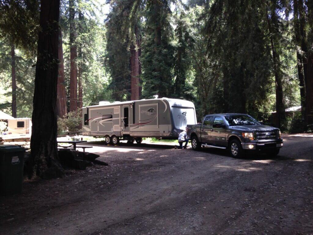 A truck towing an RV reverses the RV into the campsite using the swoop method.