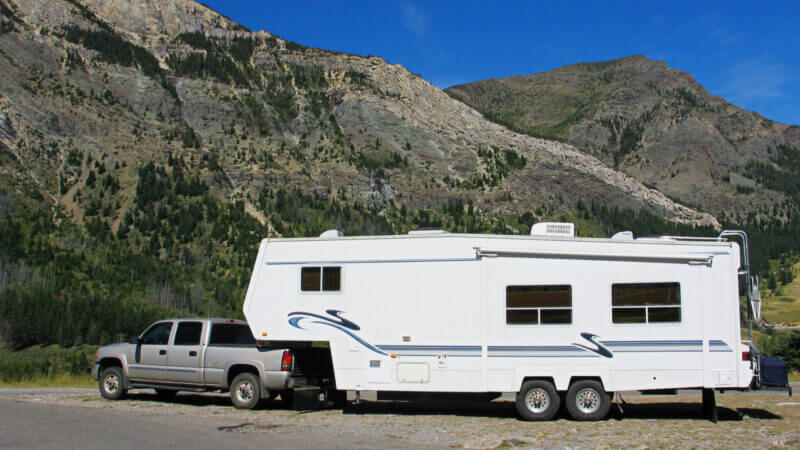 A large truck is needed to tow a fifth wheel, which is the best? This truck tows a fifth wheel alongside some brown hills.