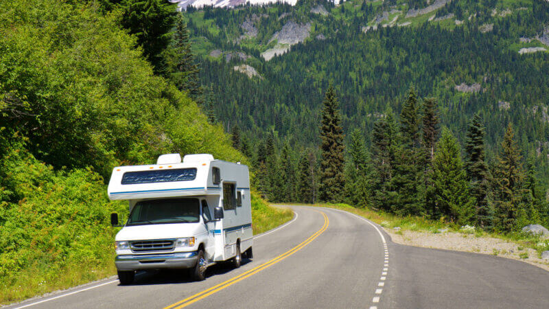Want to know how to rent an RV for a road trip? Here is a white RV driving down a mountain road in Washington state.