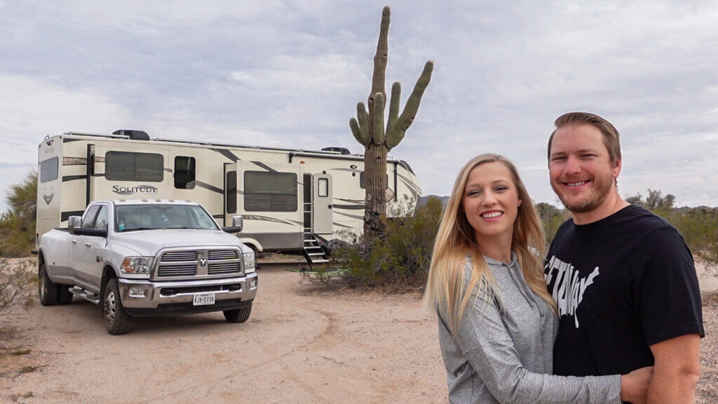 A couple standing in front of their RV and truck smiling at the camera