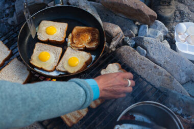 man cooking toast and eggs on a campfire