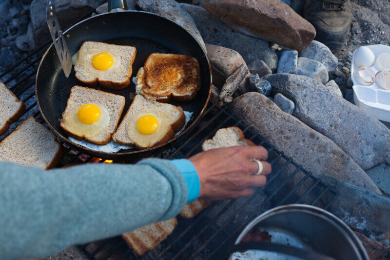 man cooking toast and eggs on a campfire