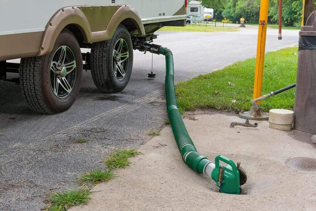 A trailer dumps their black tank using a green Lippert Waste Master sewer hose kit. 