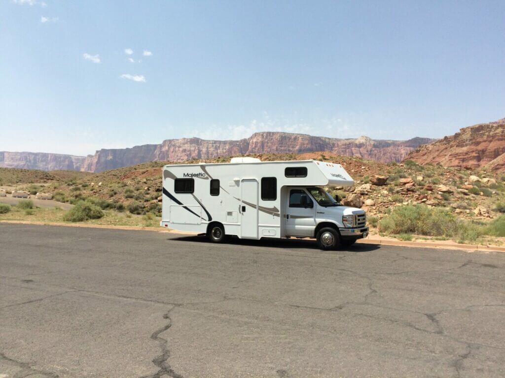 An RV parked on the side of the road in the desert with buttes in the background