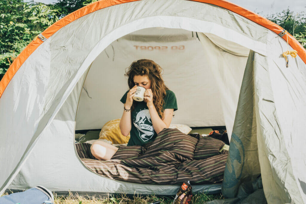 a girl drinking coffee in her tent after setting up her tent stakes