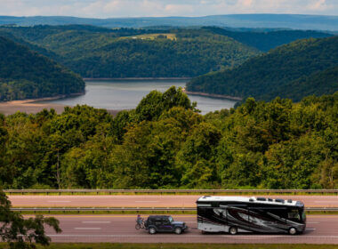 rv with slides in driving down the highway with a beautiful lake view behind it