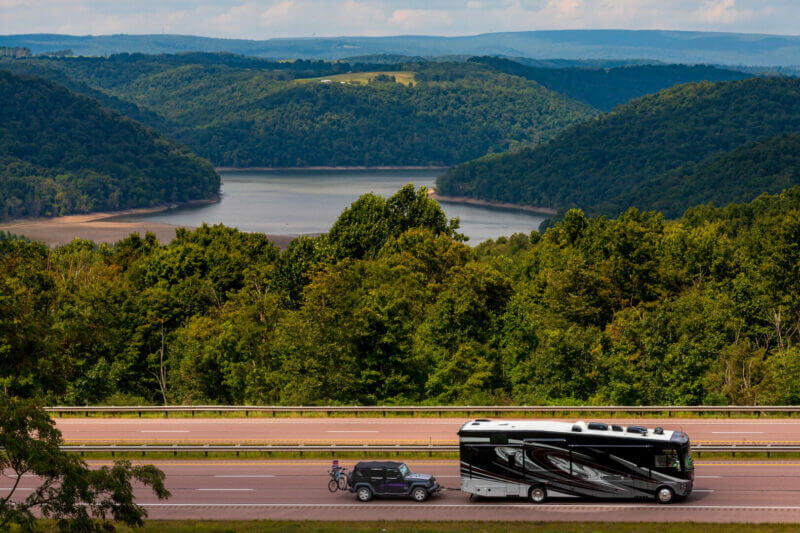 rv with slides in driving down the highway with a beautiful lake view behind it