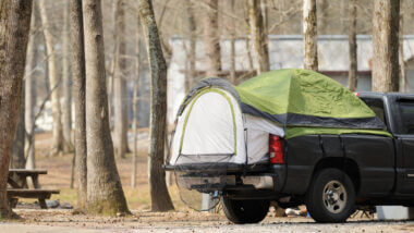 A truck is parked in a camping site with a truck bed tent in the back for convenient and comfortable camping.
