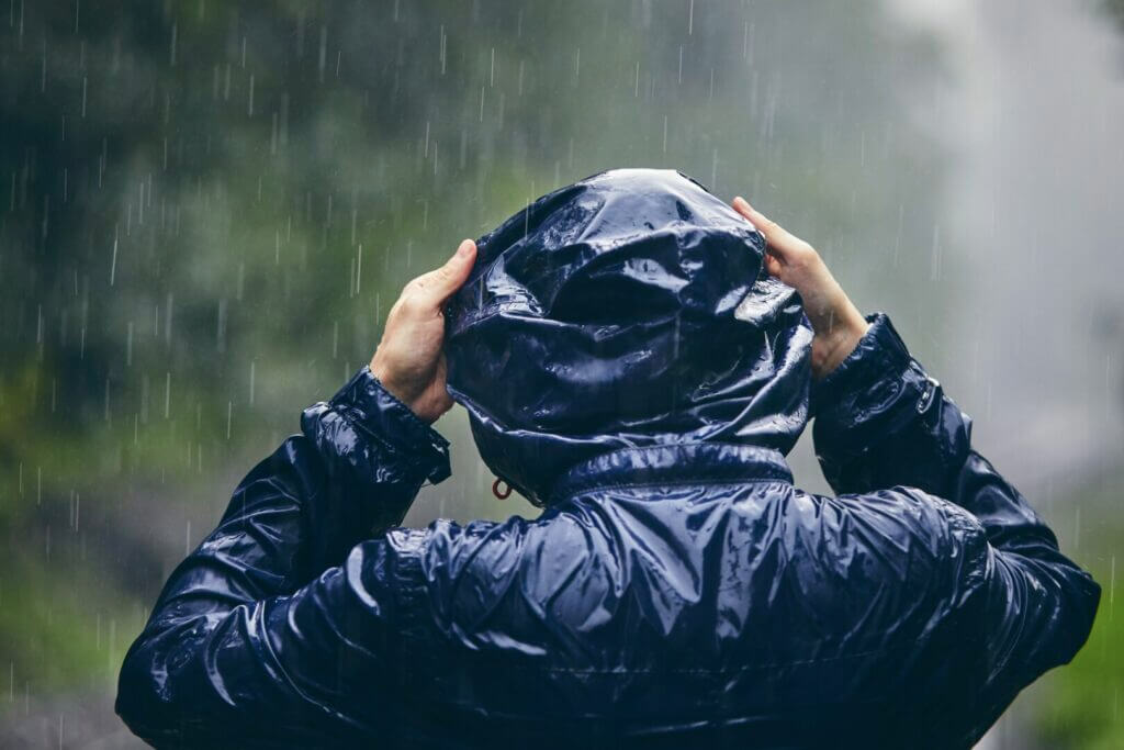 Pedestrian putting on a rain jacket during a heavy rainstorm.