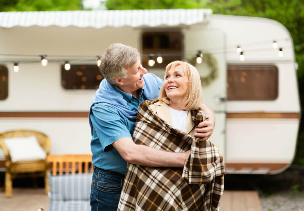 A man and woman in retirement hugging outside of their RV campsite.
