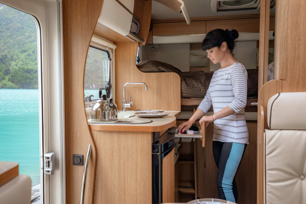 A woman cleaning her kitchen in an RV parked beside the lake.