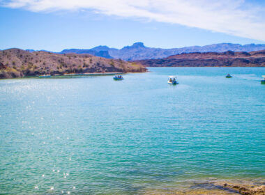 Boats sit on top of Lake Havasu and the bright blue green waters with desert mountains around.