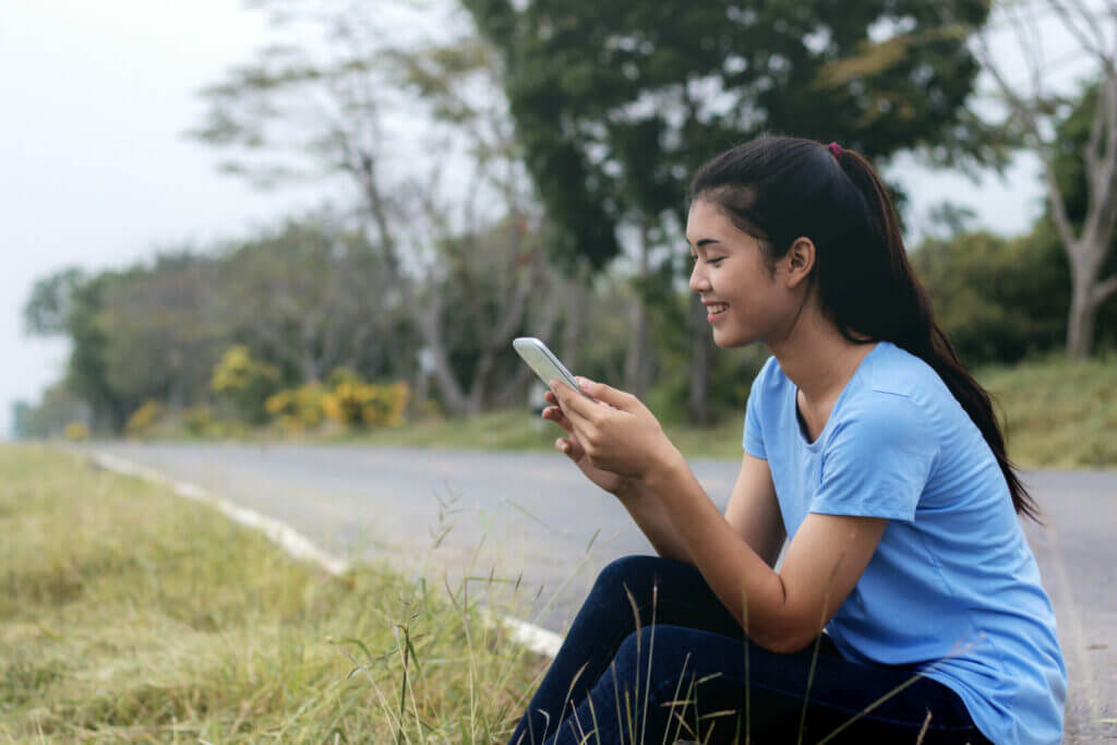 Woman sitting beside the road using cell phone.