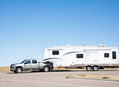 A dually truck tows a large fifth wheel trailer across a parking lot in the desert.