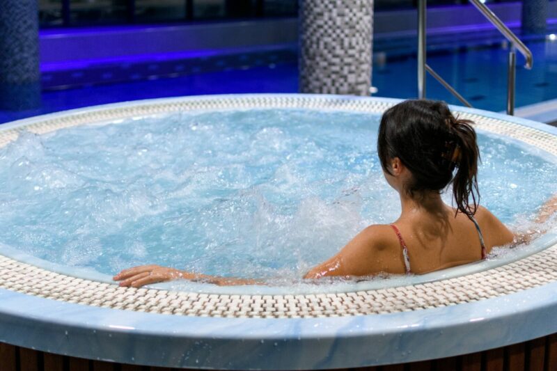 A woman relaxes in a blue hot tub all to herself.