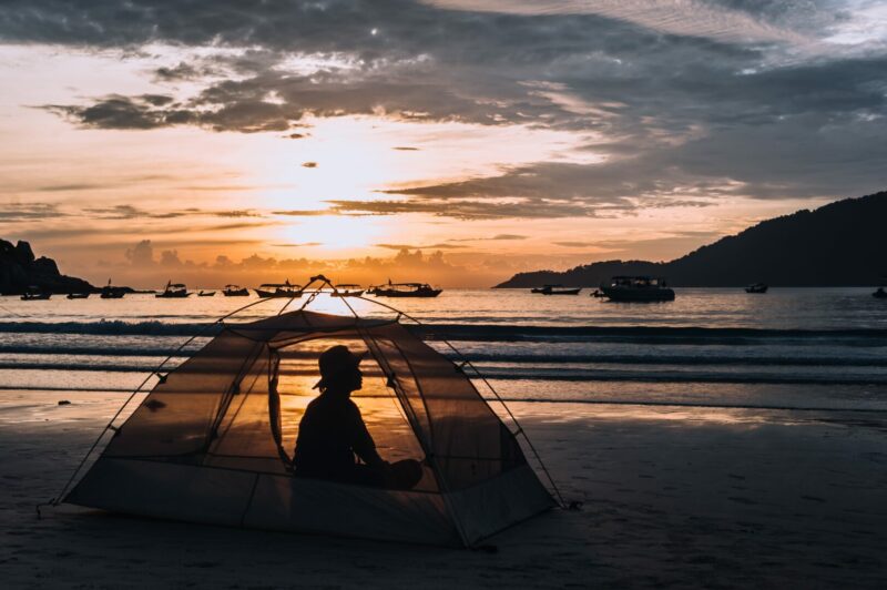 A woman sits in a tent on a beach at sunrise.