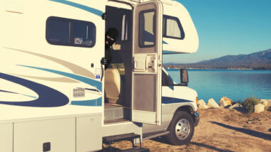 An RV is parked along water and a thief is poking his head out of the open door.