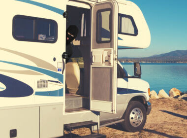 An RV is parked along water and a thief is poking his head out of the open door.