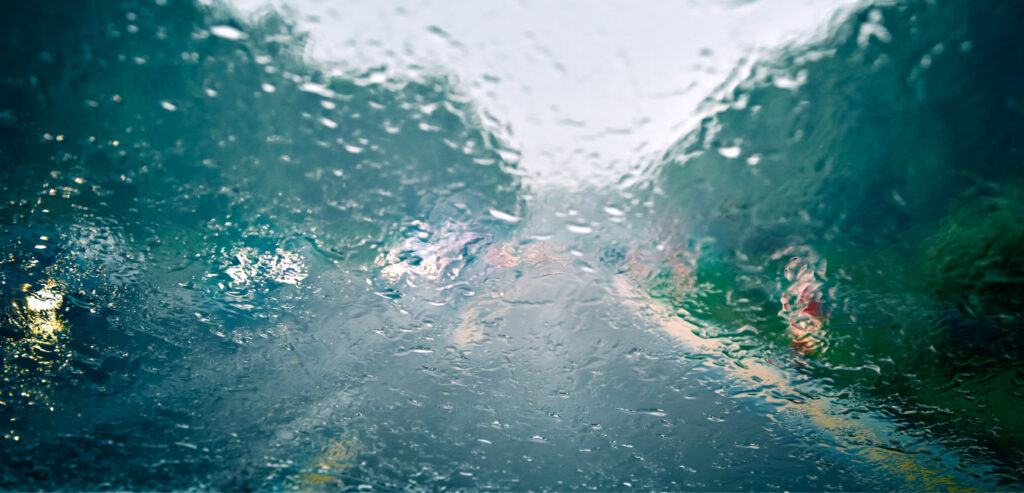Rain hitting a car windshield along a highway. 