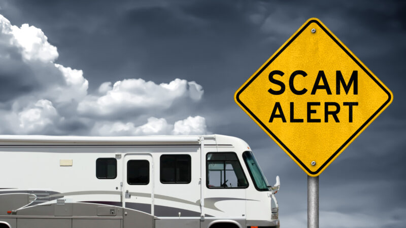 A used motorhome RV set against a dark cloudy sky with a scam alert sign.
