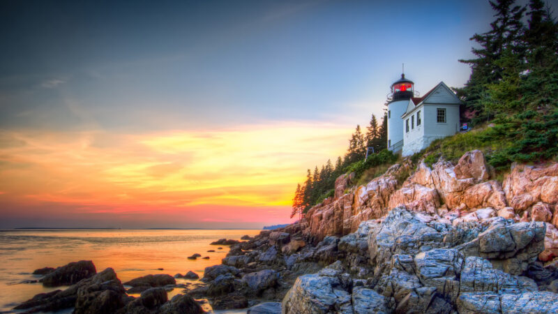 The sunset glows on Bass Harbor lighthouse and the coast of Bar Harbor, Maine.