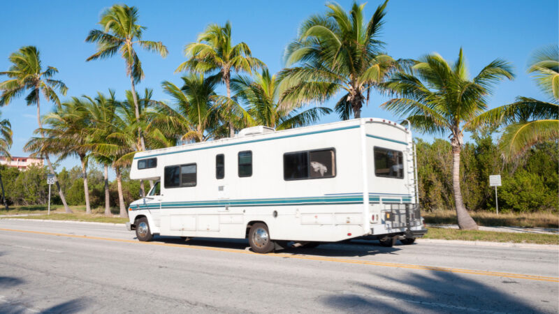 An RV is driving down a palm tree lined street in Florida.