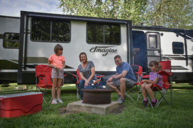 A family enjoys a campfire in front of their Grand Design Imagine travel trailer.