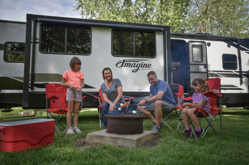 A family enjoys a campfire in front of their Grand Design Imagine travel trailer.