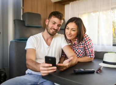 A couple looks at free camping apps on the man's phone while sitting at the table inside their RV.