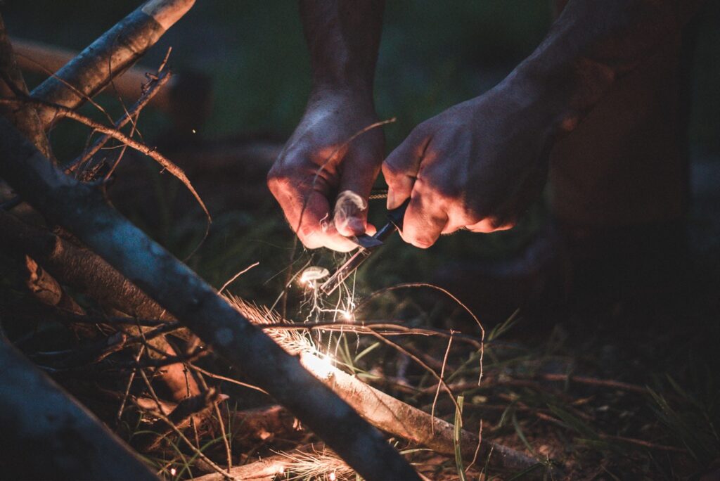 a man using a campfire starter over some loose leaves and wood