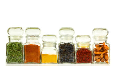 Spices lined up together in jars against a white backdrop.