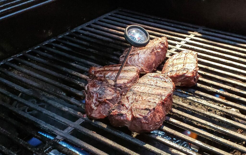 A steak that has been grilled by campfire cooking, with a meat thermometer sticking out of it