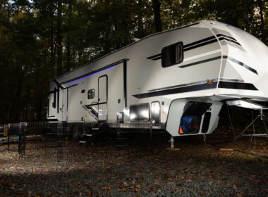 A fifth wheel toy hauler lit up in a dark camping spot.