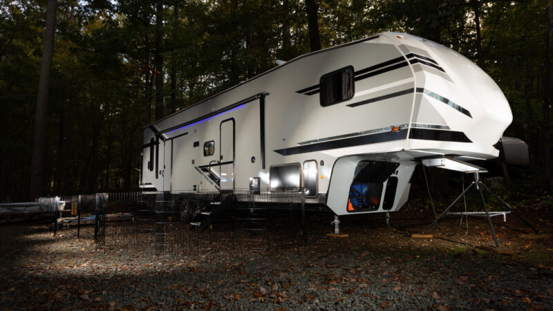A fifth wheel toy hauler lit up in a dark camping spot.