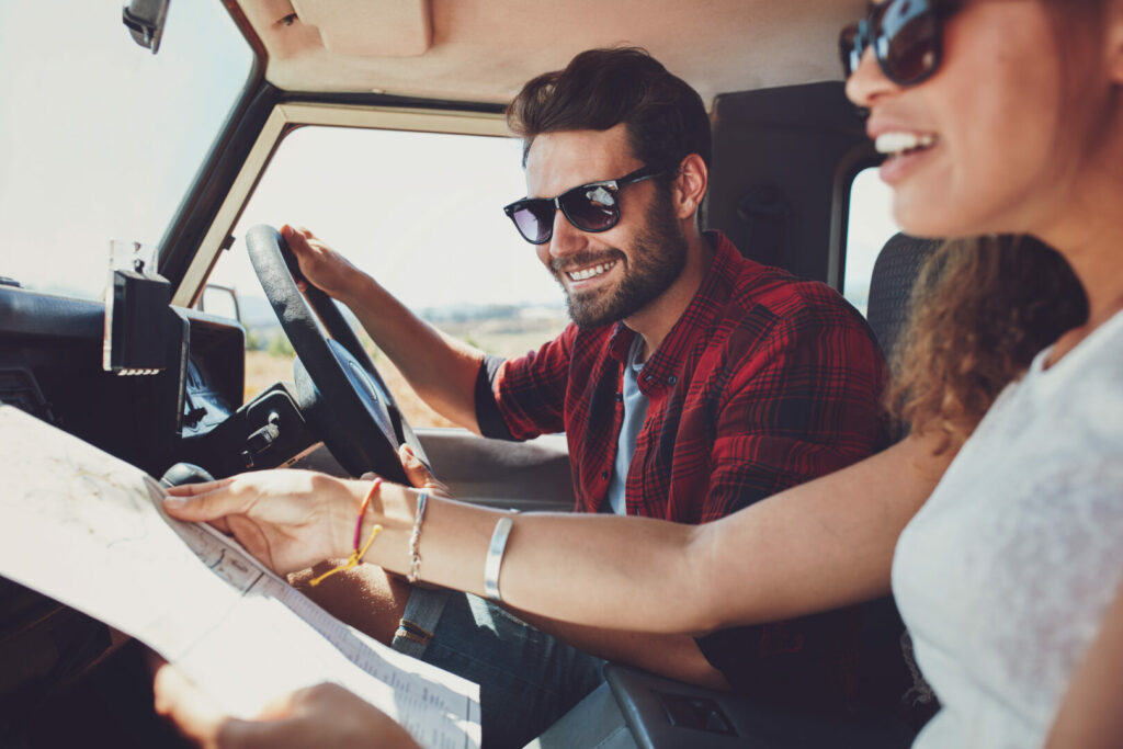 Smiling young man driving the car with woman holding a road map. Young couple on road trip.