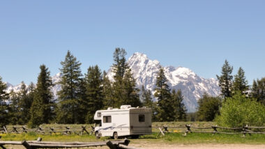 A lone RV is boondocking on open land in Wyoming with mountains and trees in the background.