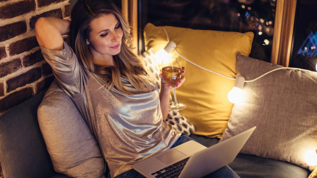 A woman relaxing with a glass of wine watching her favorite streaming service on her laptop.