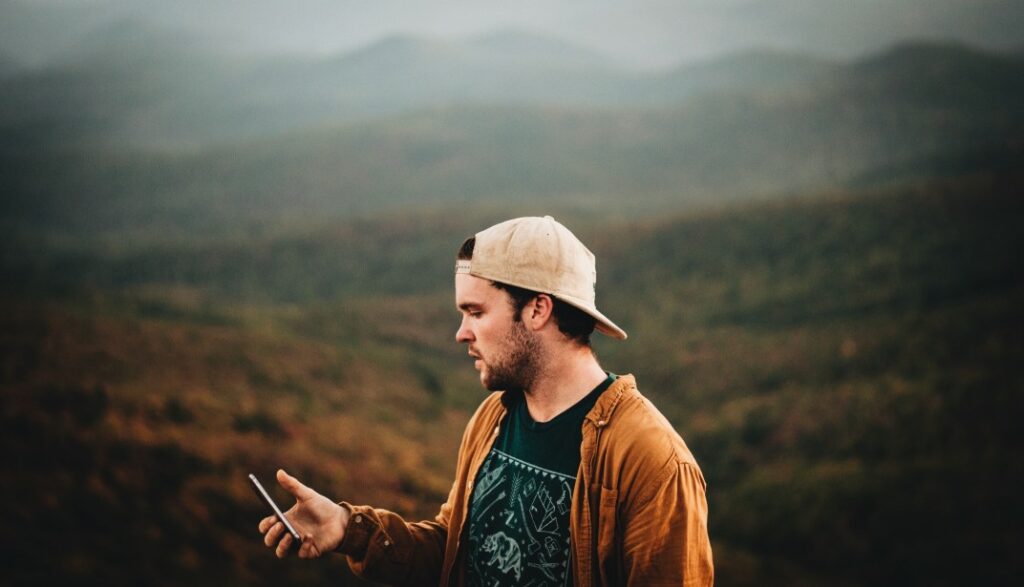 A man in the mountains during a cloudy fall day holds out his cell phone in search of cell signal—one of many boondocking must-haves he forgot to consider.