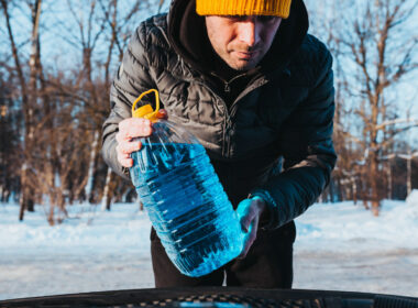 Man outside in cold weather prepares to pour blue antifreeze from a RV winterizing kit
