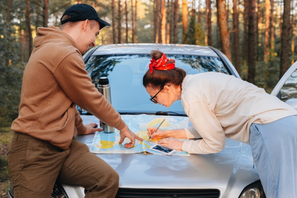 Man and woman leaning over a map and smart phone on top of a vehicle hood practicing the planning step of boondock safety