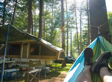 Shot of feet in a hammock with pop up camper in the background and the sun streaming through the trees