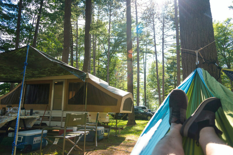 Shot of feet in a hammock with pop up camper in the background and the sun streaming through the trees