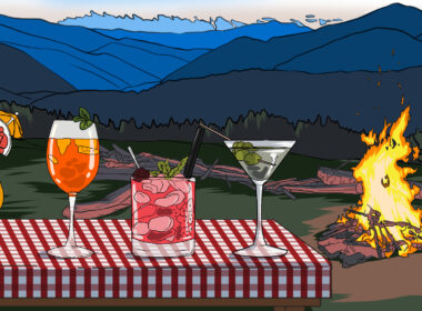 Camping cocktails sitting on a picnic table with a campfire in the background