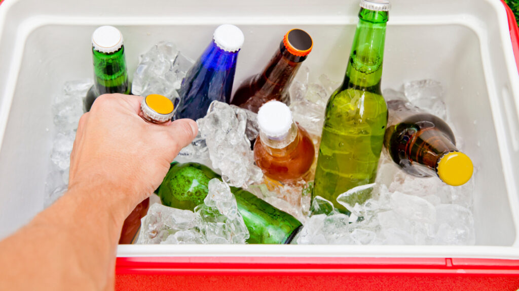 A hand grabs a beer out of a full and cold ice filled cooler.