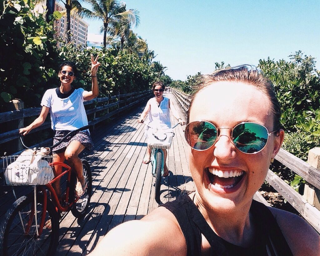 Woman takes a selfie with her friends as they bike down the boardwalk in a tropical beach town.