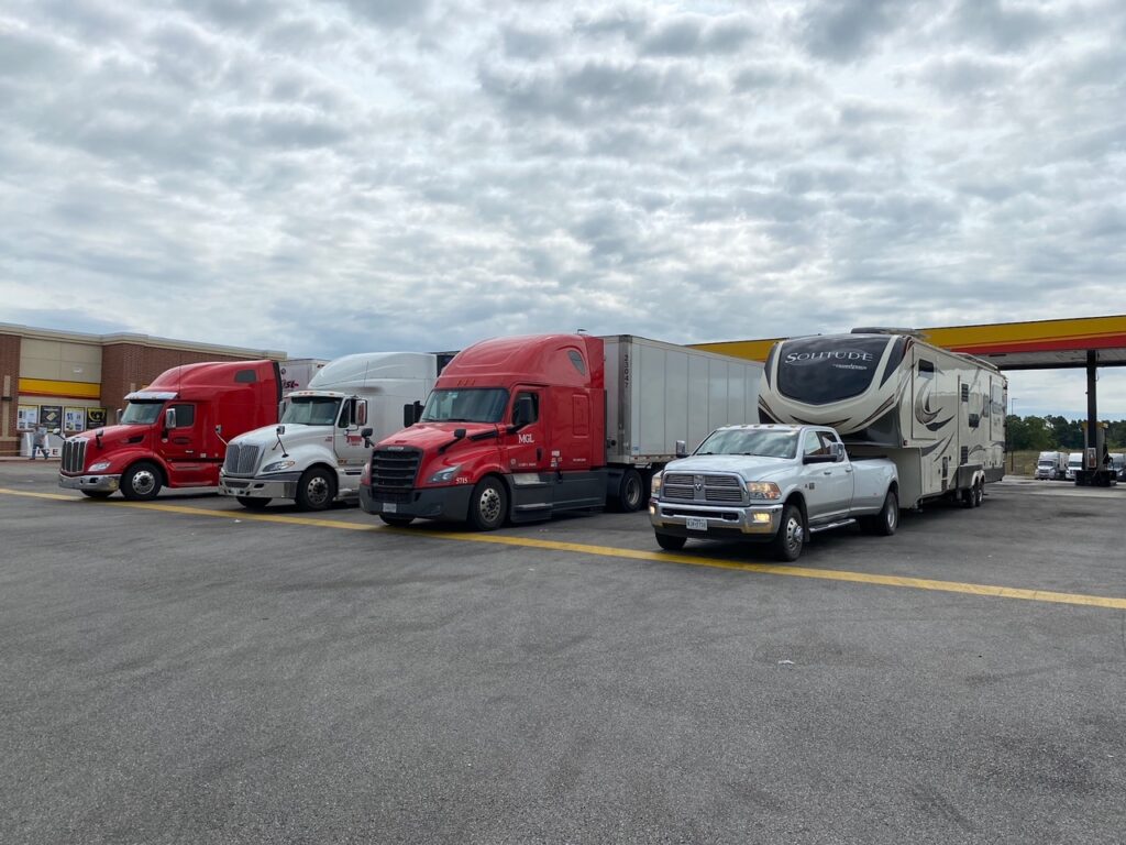 An RV is pulled forward and parked next to trucks at a truck stop gas station.