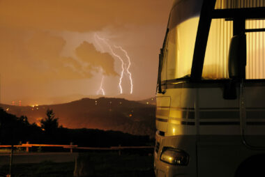 Motorhome in campground at night with lightning storm in background