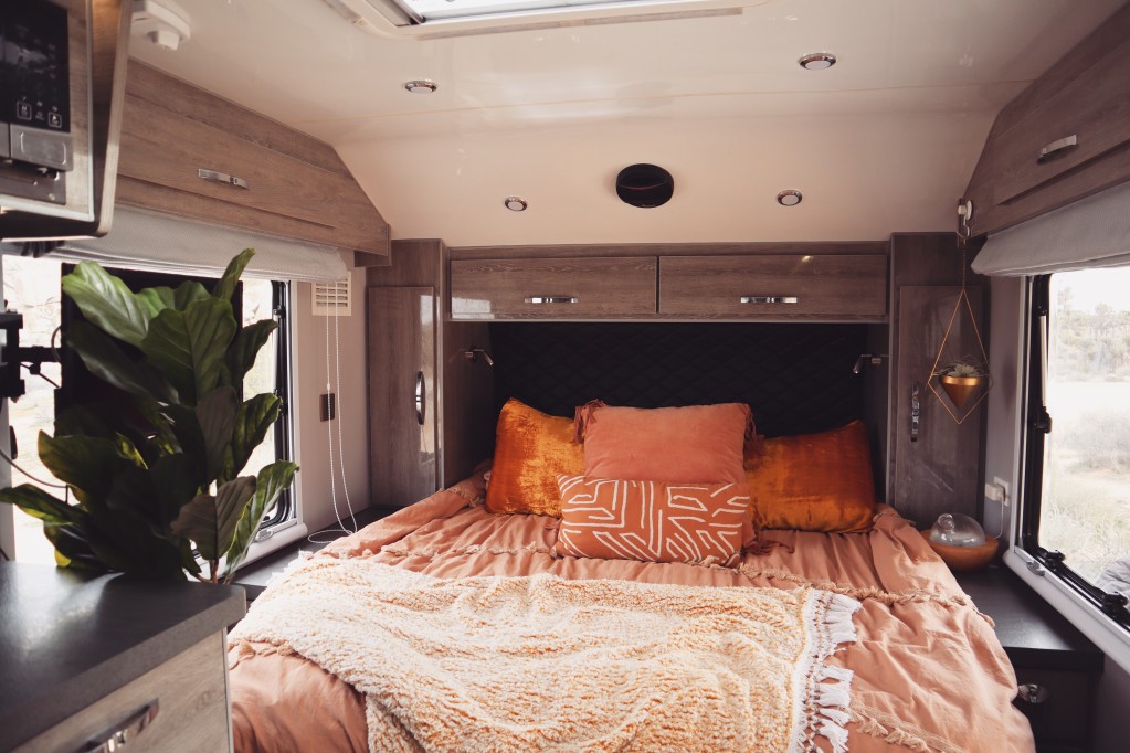 An upgraded bedroom of a trailer trailer with sleek gray storage cabinets and bright orange bedding.