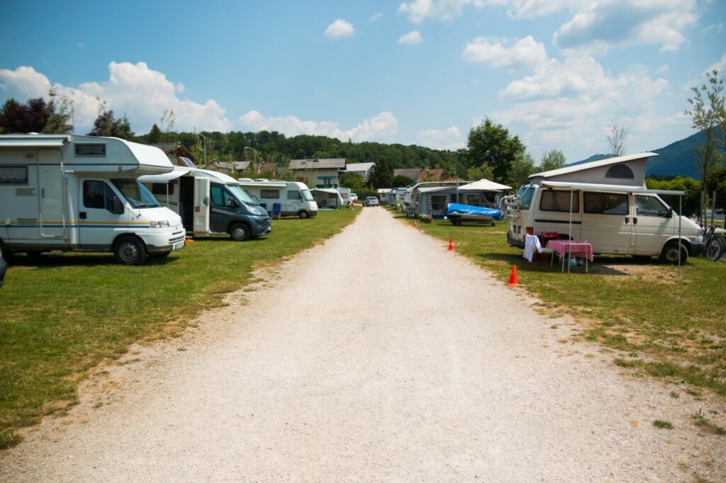 A grassy campground with many different RVs parked in a row along a gravel road.